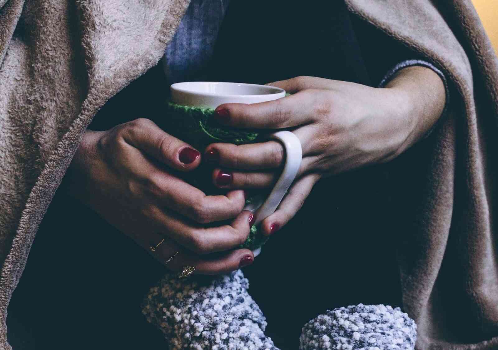 Woman with chronic pain holding a coffee cup and wrapped in a blanket.