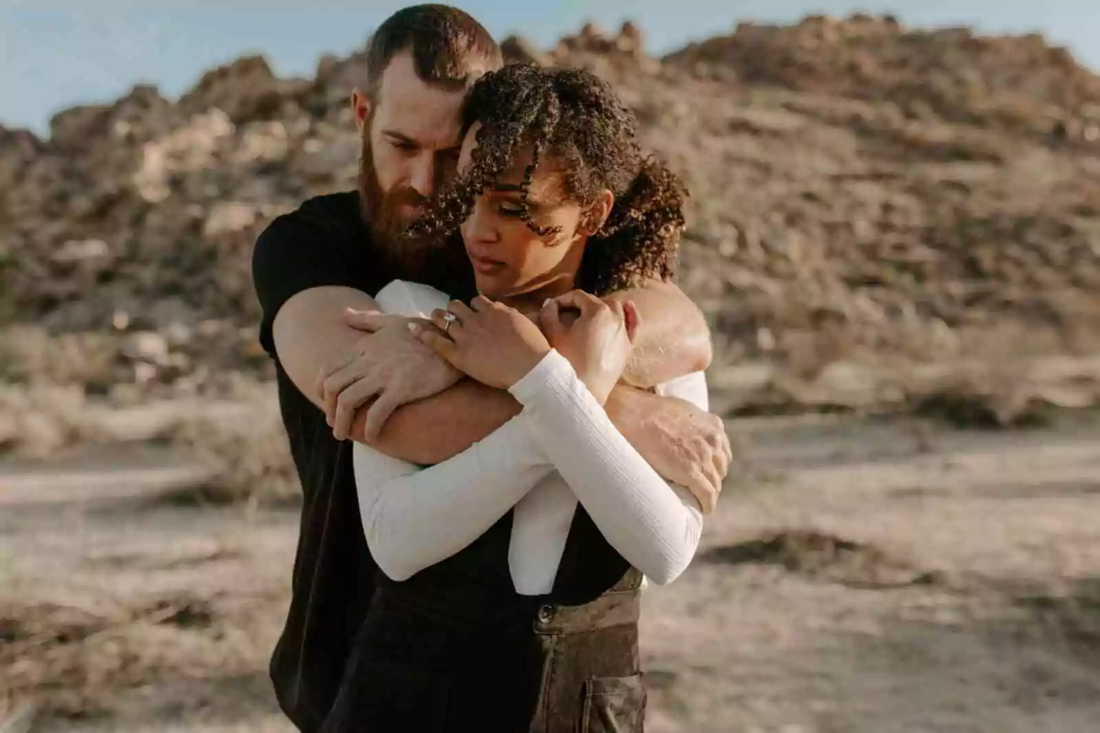 Dating with a chronic illness: White man embracing Black woman outdoors in a rocky landscape.