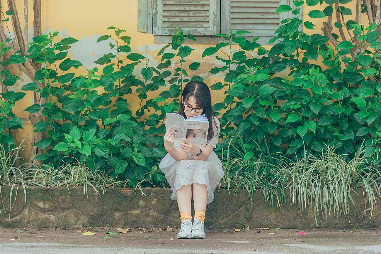 Children's books about disabilities - a young Asian girl sitting in the garden reading a book.