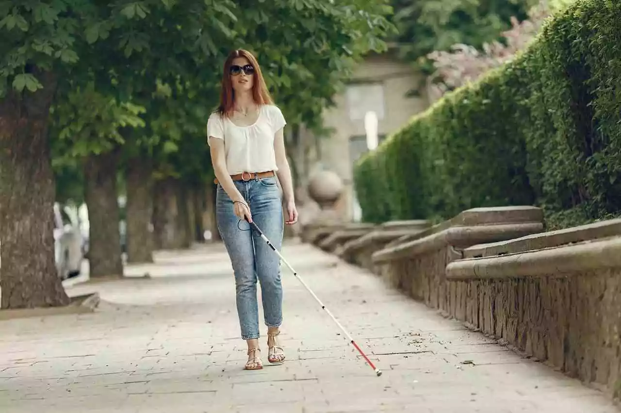 White canes for blindness -- Woman with low vision using a white cane for orientation and mobility outdoors on sidewalk.