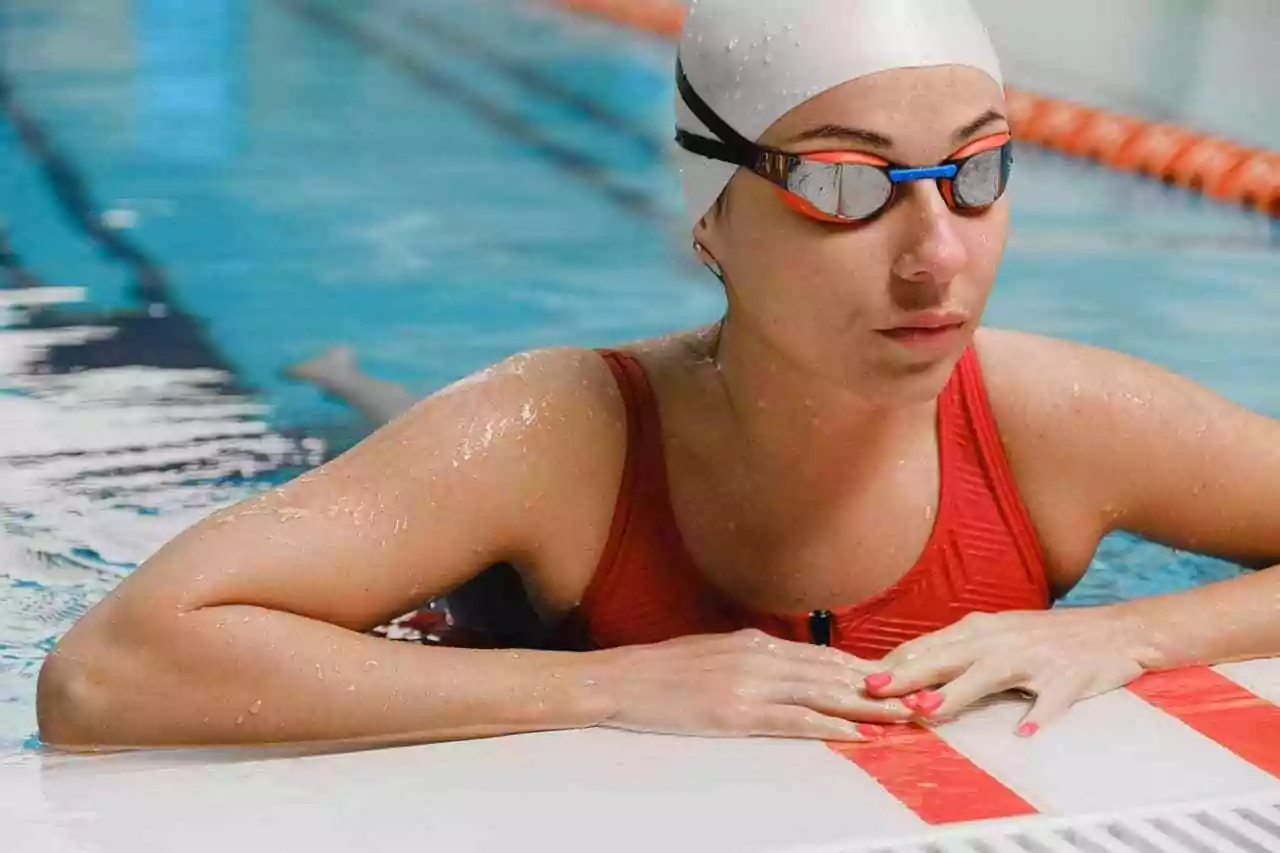 Sports for blind people: Woman swimming in a pool, wearing red swimsuit and goggles.