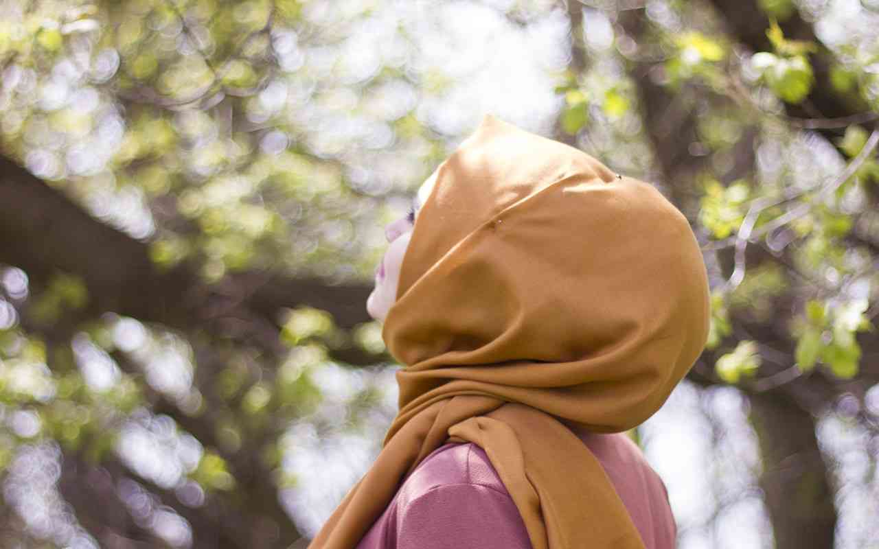 Religious fasting and eating disorder recovery. Muslim woman in a gold head scarf looks up at a tree.