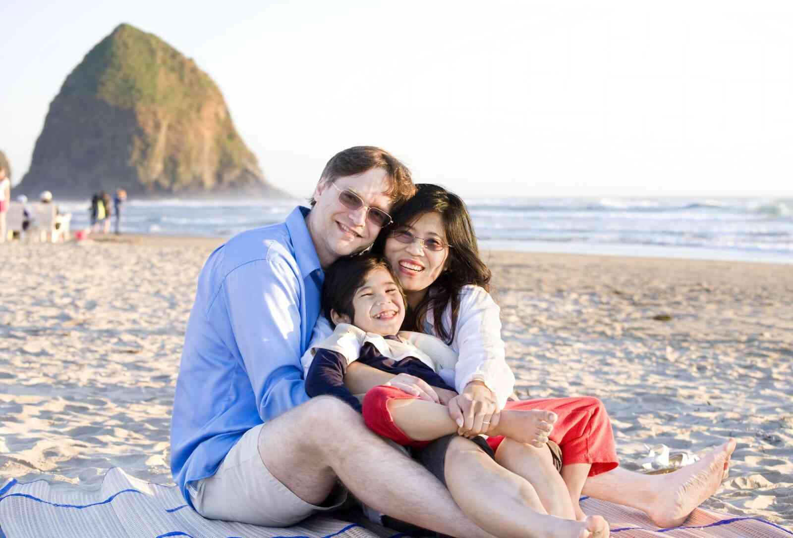 Little boy with cerebral palsy and his parents sitting at the beach by the ocean.
