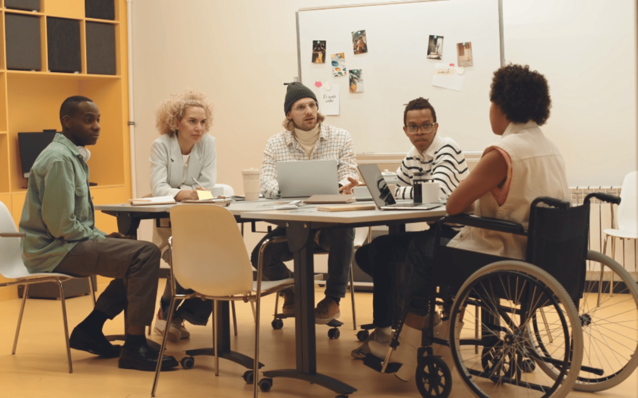 DEI Diversity, Equity, and Inclusion often excludes disability. Group of diverse work colleagues including a Black woman who uses a wheelchair.