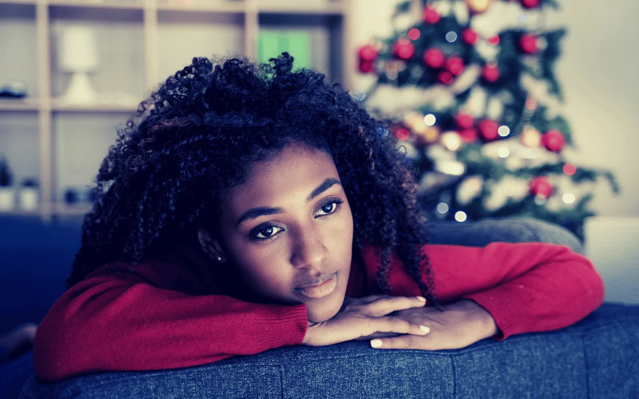 Coping with grief during the holidays. A Black woman looks sad with a Christmas tree in the background.