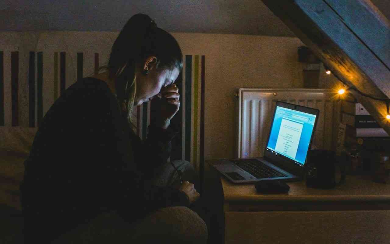 Working while managing ankylosing spondylitis and other chronic illnesses. A tired woman at a laptop computer in a dark room.