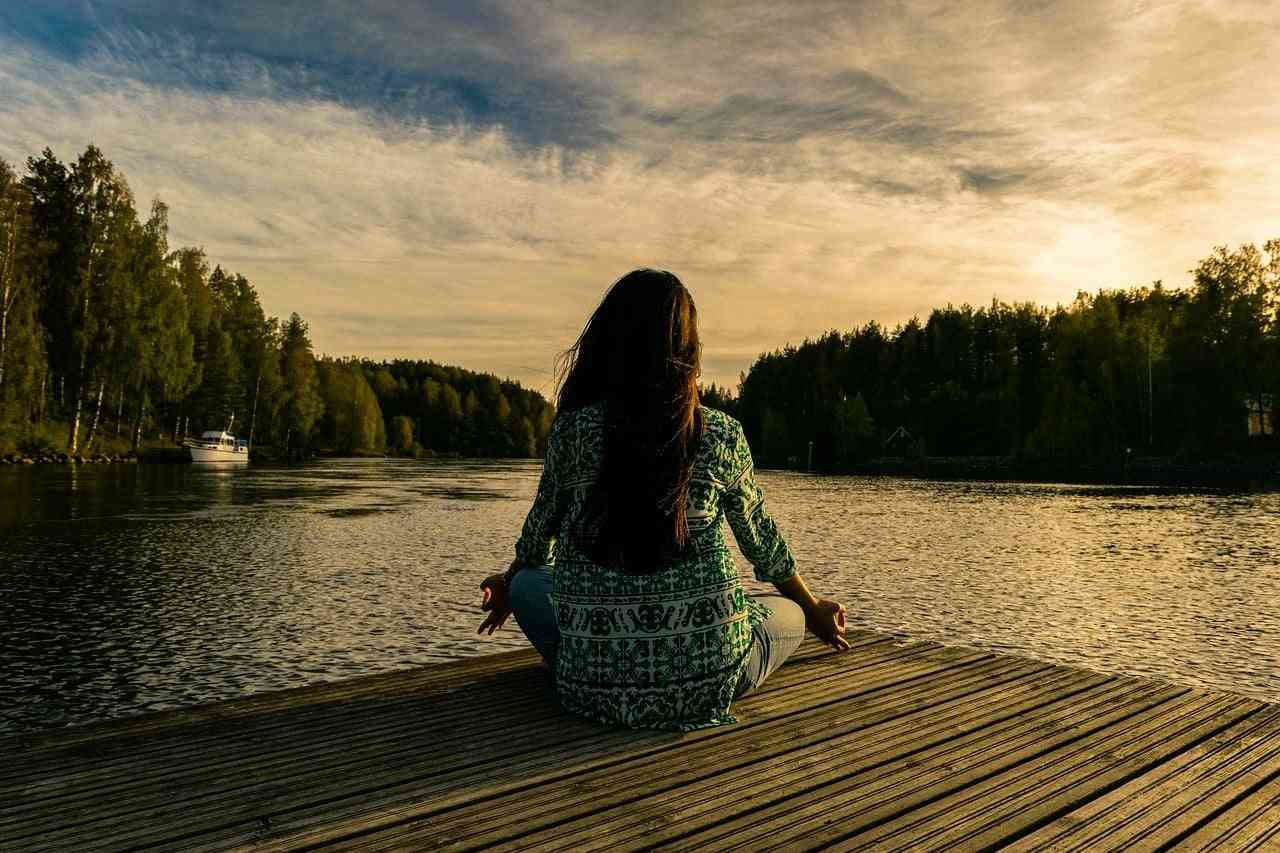 How mindfulness can help people with chronic illness. Woman sitting on a dock practicing meditation.