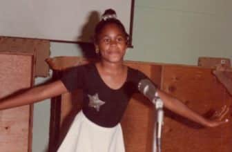 Alisa as a child, wearing a ballet dress and standing at a microphone.