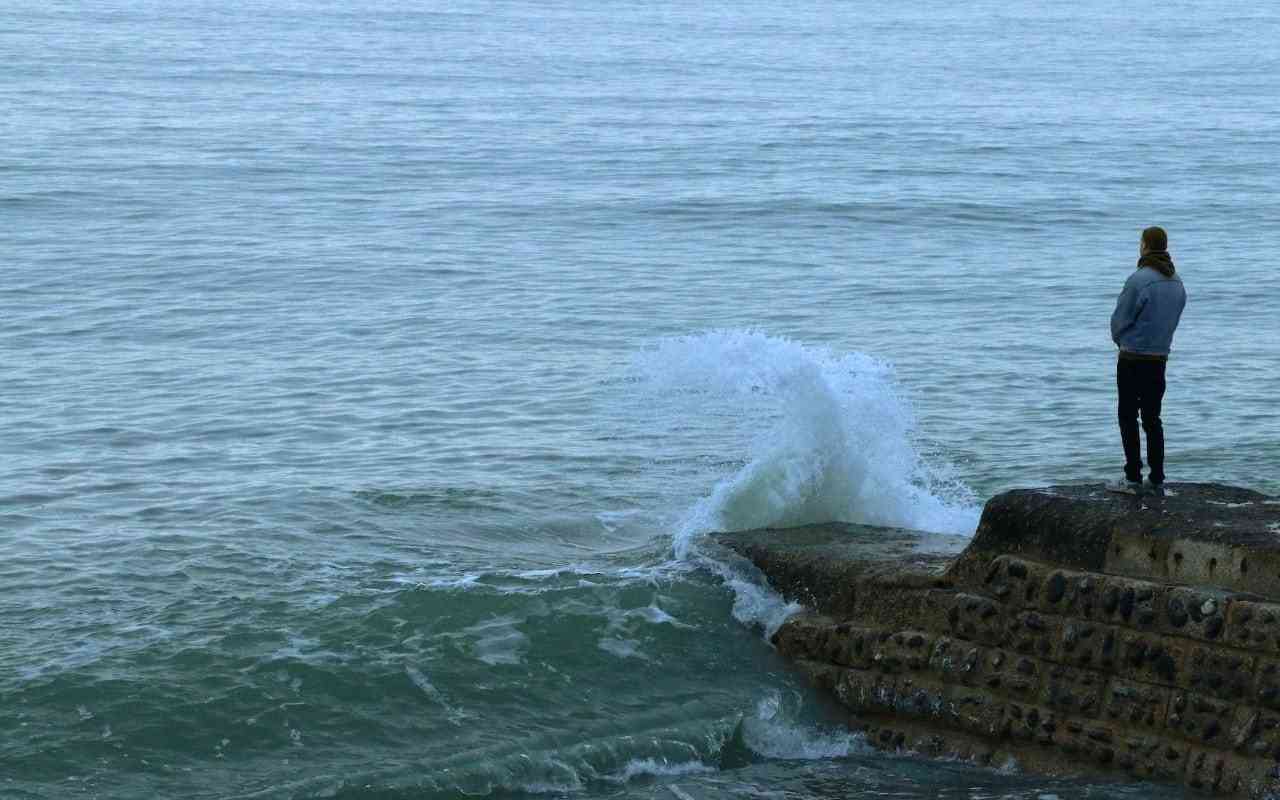 Climate change and mental health. Man looking at rising ocean waves.