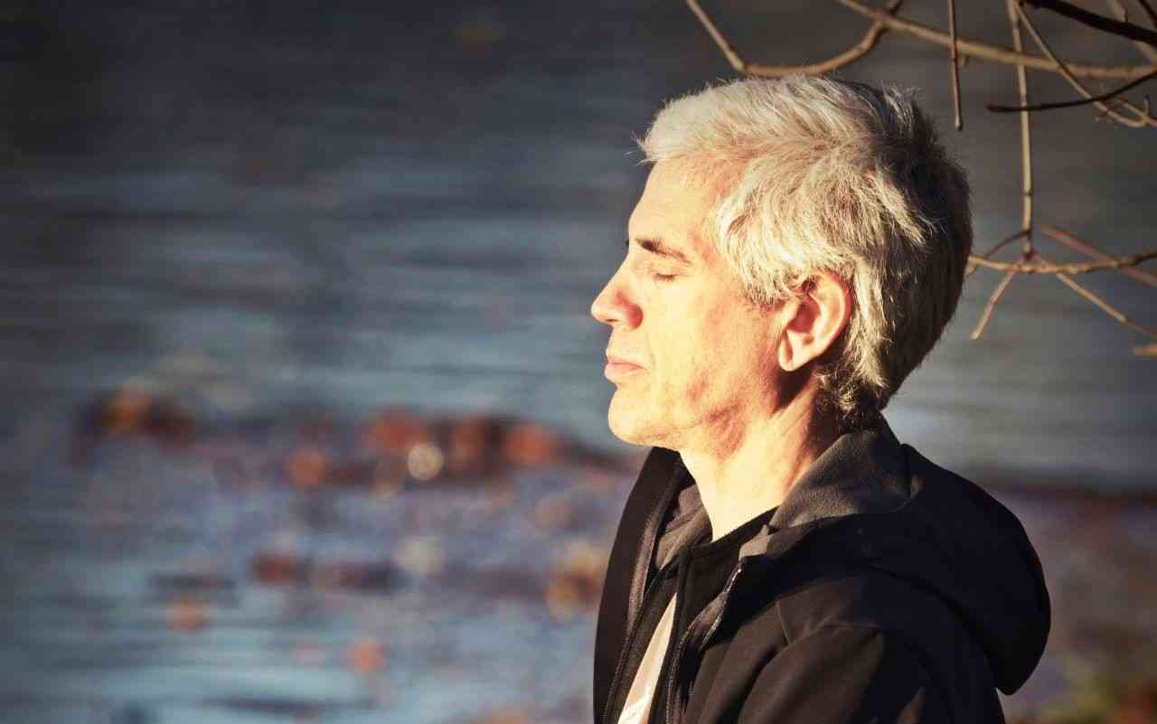 How mindfulness can improve your mental health. Man sitting by a lake meditating.