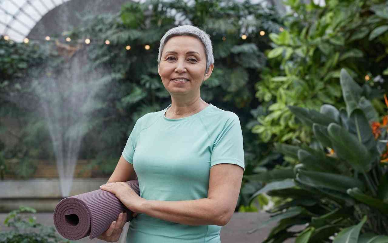 Older woman holding yoga mat.