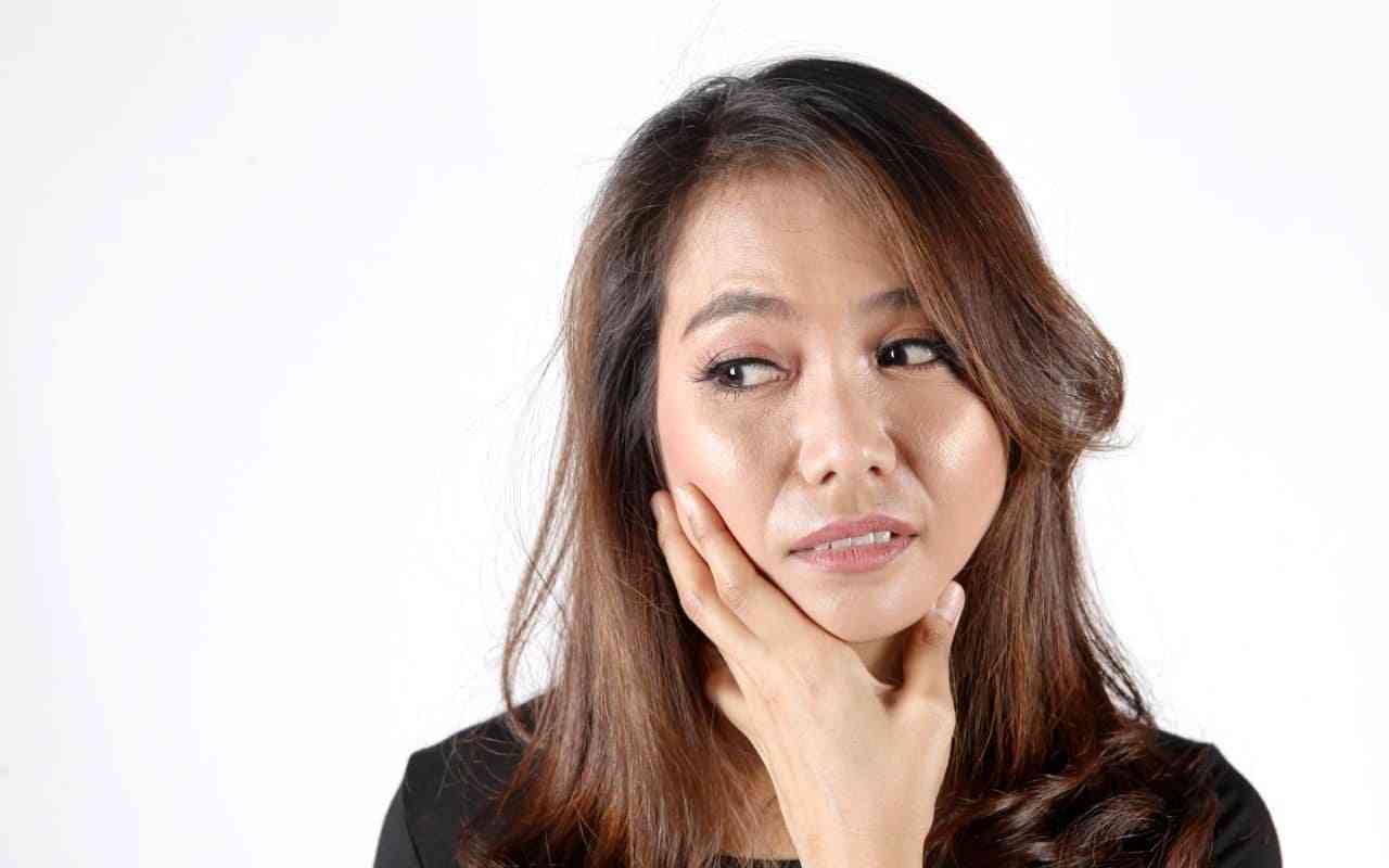 Jaw surgery and mental health. A woman holds her jaw while looking thoughtful.