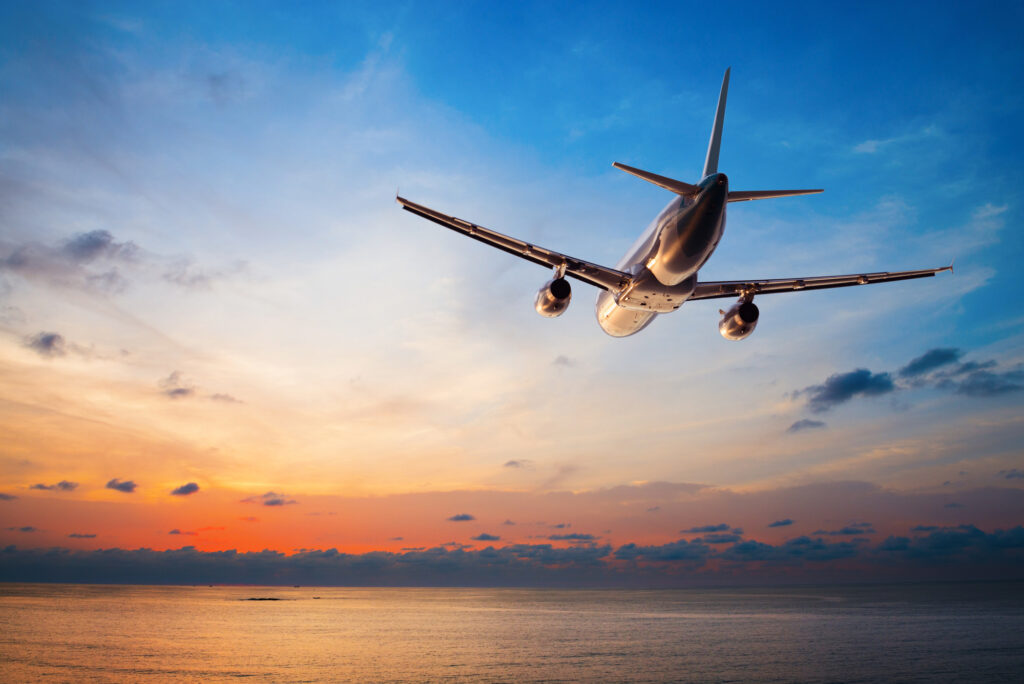 Airplane flying over ocean at sunset.