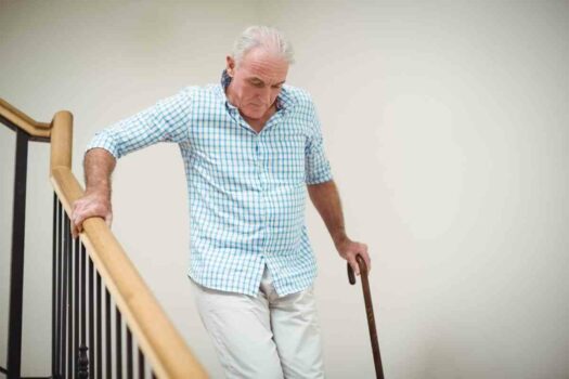 Senior man with disability and cane struggling to use stairs.