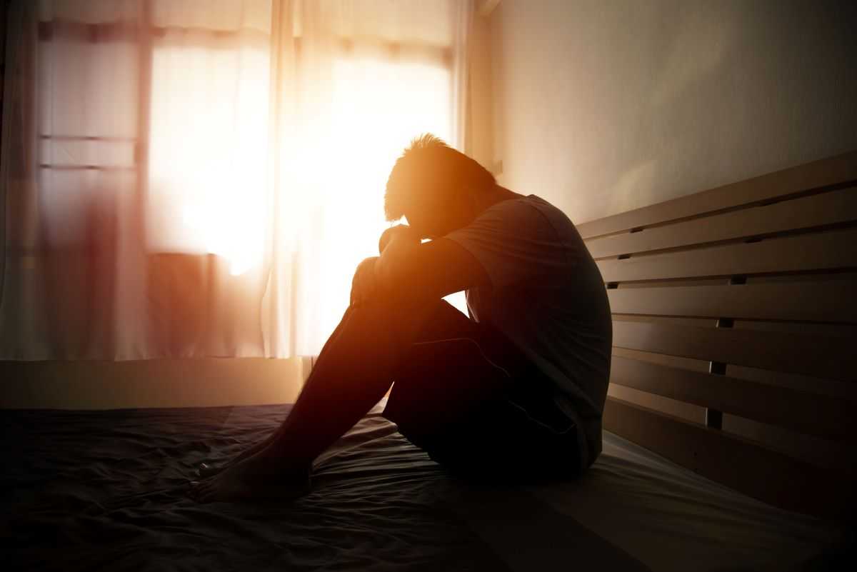 Man struggling with addiction sitting in bed holding his head in his hands.