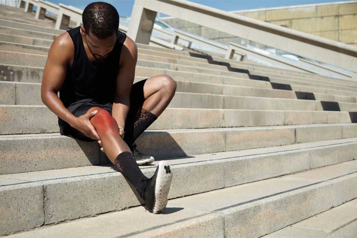 Man sitting on steps holding his injured knee.