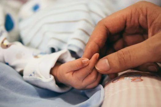 Woman's hand holding newborn baby's hand.