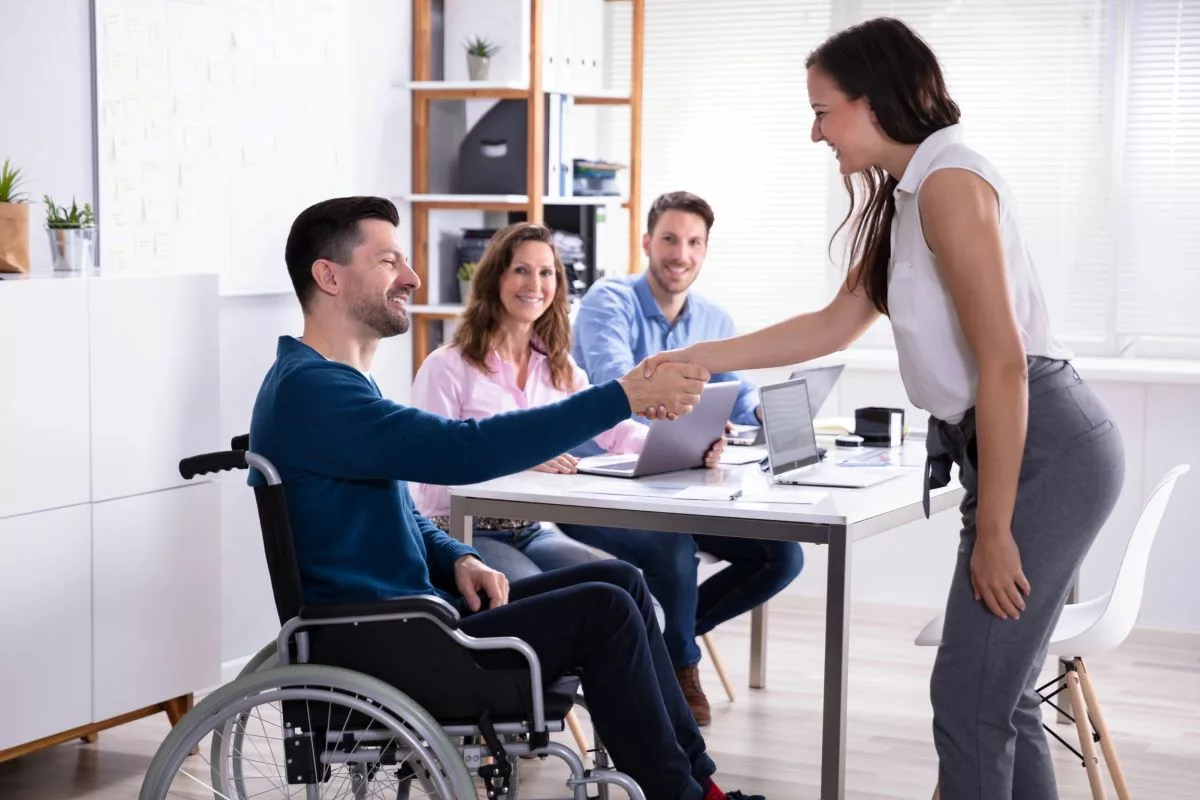 Man in wheelchair shaking hands with woman.