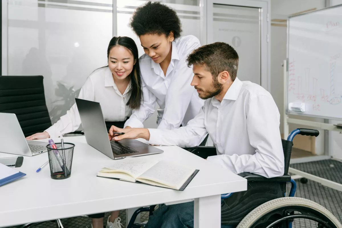 Man in wheelchair with colleagues looking at computer.