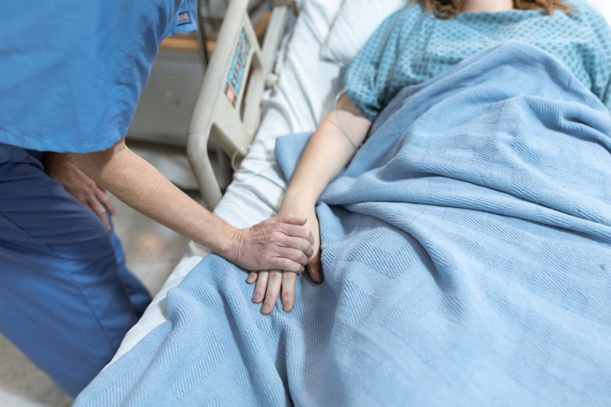 Nurse holding patient's hand in hospital bed.