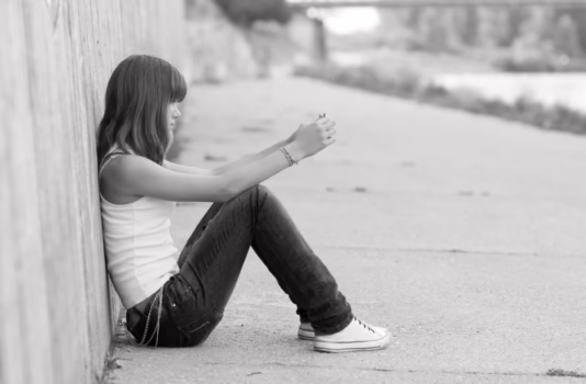 Sad teen sitting by a wall.
