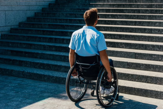 Seeking compensation for ADA violations is justice, not profiteering. Man in wheelchair facing a flight of stairs.